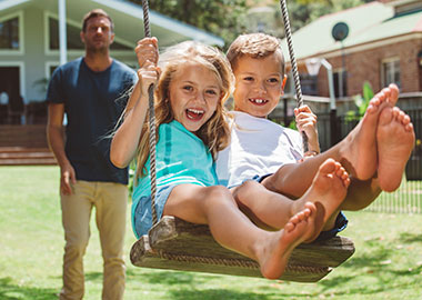 Dad pushing two kids on swing in backyard.