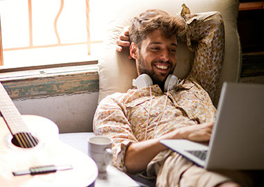 Guy at home on couch using laptop.