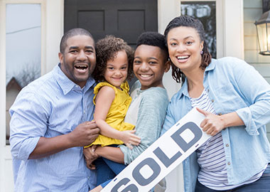 Parents and two kids with sold sign in front of house.