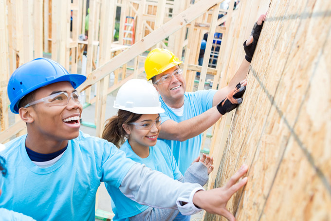 Three smiling volunteers working on construction of a home